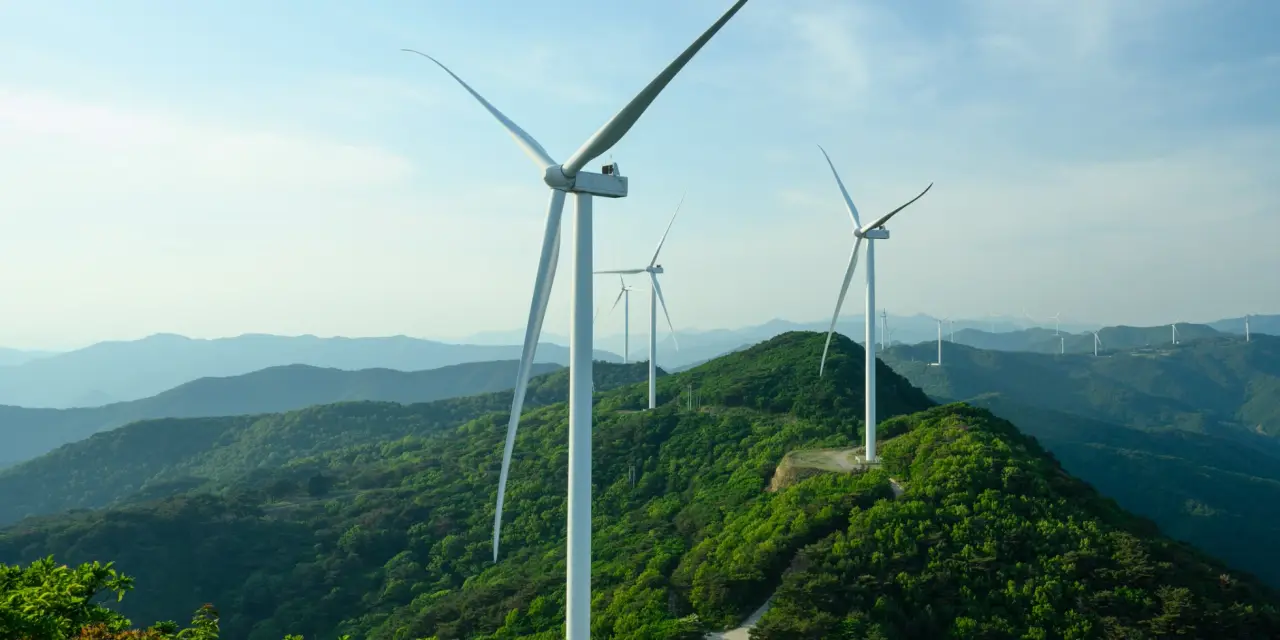 A wind turbine and its rotor above a forested mountain ridge