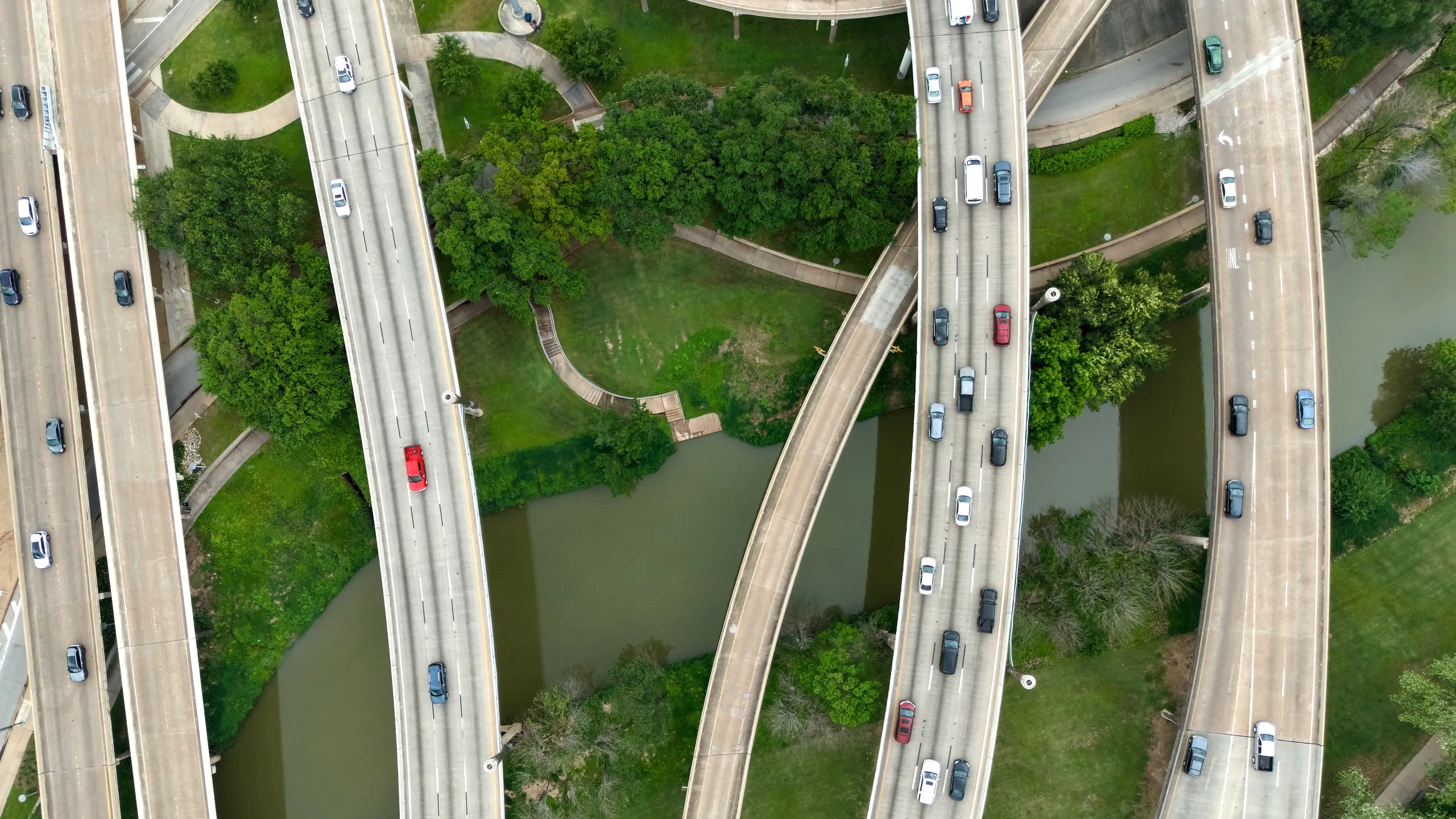 Elevated motorway viaducts carrying traffic over water and trees, seen from above